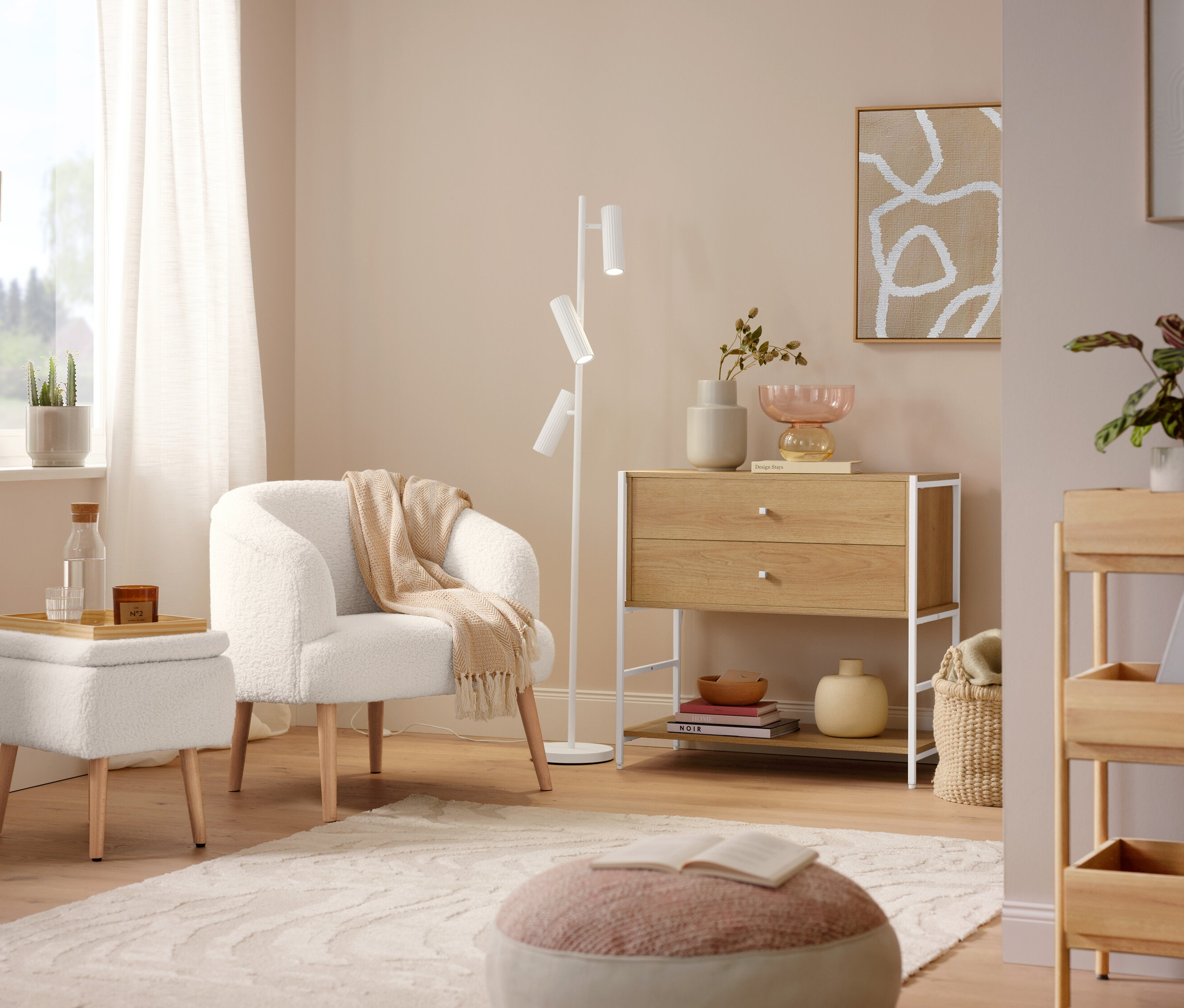 Fotel z tkaniny bouclé z drewnianymi nogami stoi obok lampy podłogowej Trio »Soka«. Na podłodze leży szary dywan »Cosmo «Waves.