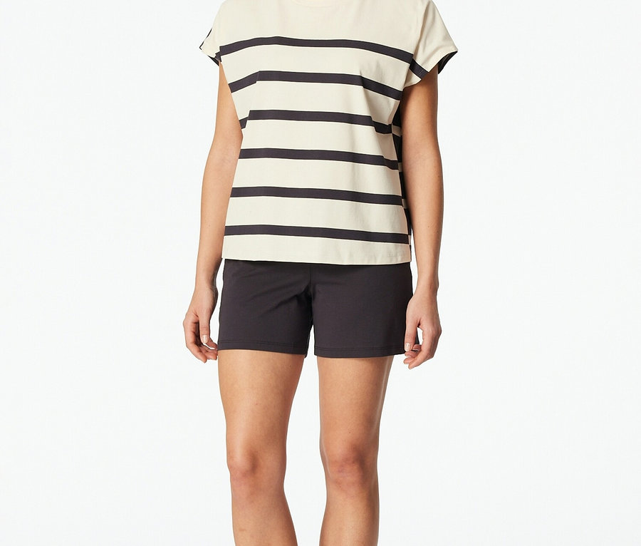 Kobieta stoi boso na białym tle w bluzce w paski i czarnych szortach.