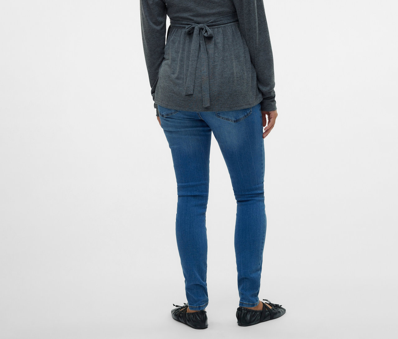 Widok z tyłu kobiety w szarej bluzce z wiązaniem i dżinsach skinny MAMALICIOUS „MLMILA” na białym tle.