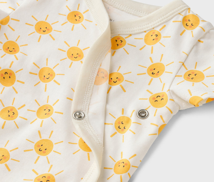 Zbliżenie białego body dziecięcego w żółte słoneczka, zapinane na zatrzaski.