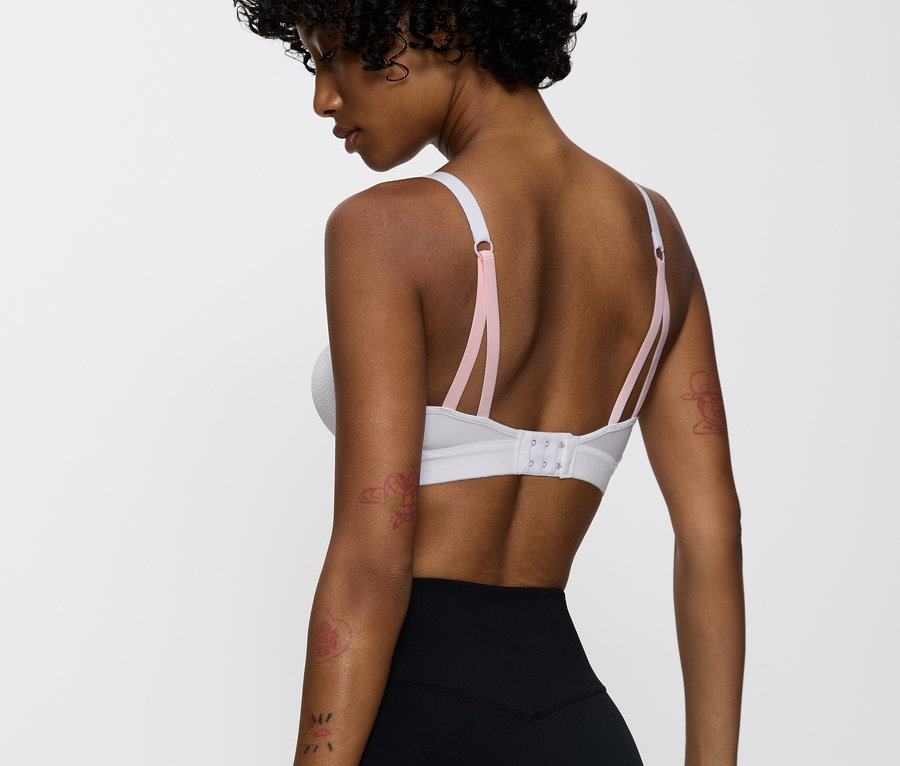 Kobieta ma na sobie biały biustonosz sportowy z różowymi ramiączkami i czarne legginsy.