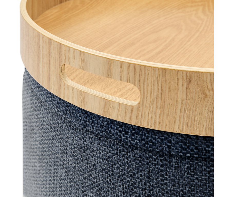 Okrągły mebel z jasnym drewnianym blatem w formie tacy i ciemnoniebieską, teksturowaną podstawą z tkaniny. Drewniany blat ma wycięty uchwyt.