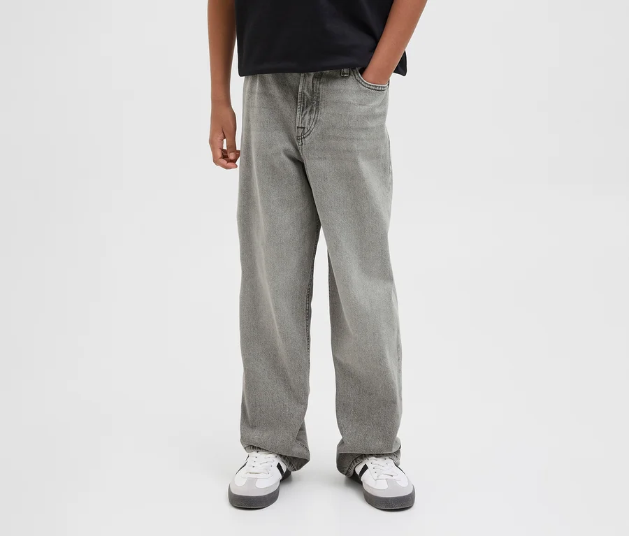 Osoba w szarych jeansach Jack&Jones JJOrginial Alex i białych sneakersach. Jedna ręka w kieszeni.
