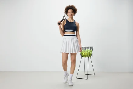Kobieta trzyma rakietę tenisową i ma na sobie niebieską sportową braletkę „Crop Top”.