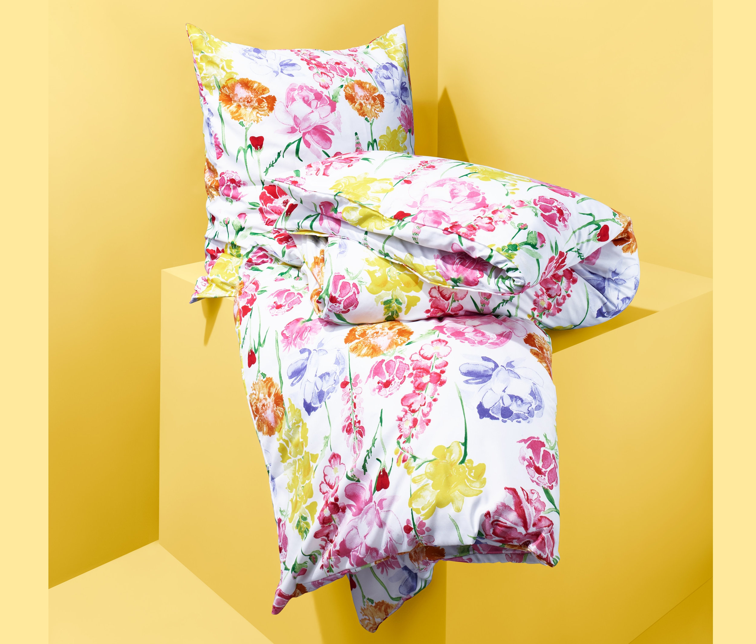 Złożona pościel z mikrowłókna we wzory kwiatowe leży na żółtym cokole.