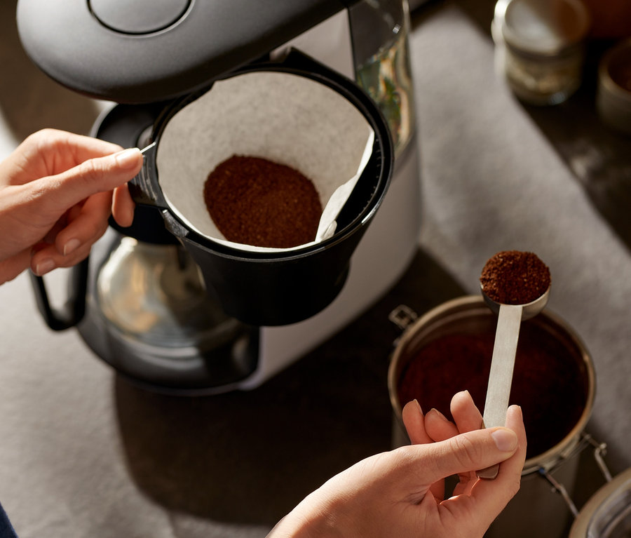 Kobieta wsypuje kawę do białego ekspresu przelewowego »Let's Brew«.