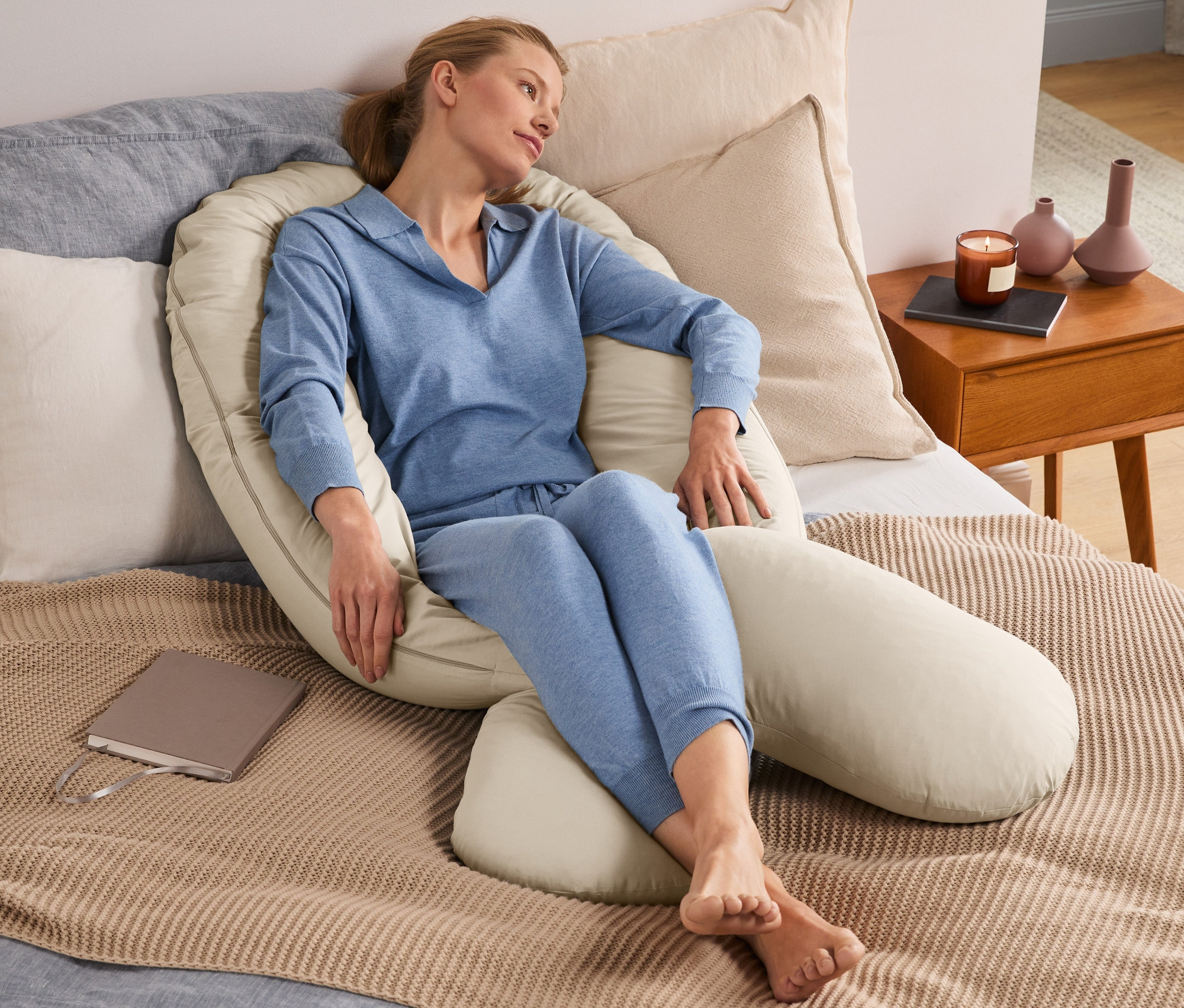 Kobieta siedzi w łóżku otoczona poduszką wielofunkcyjną XXL.