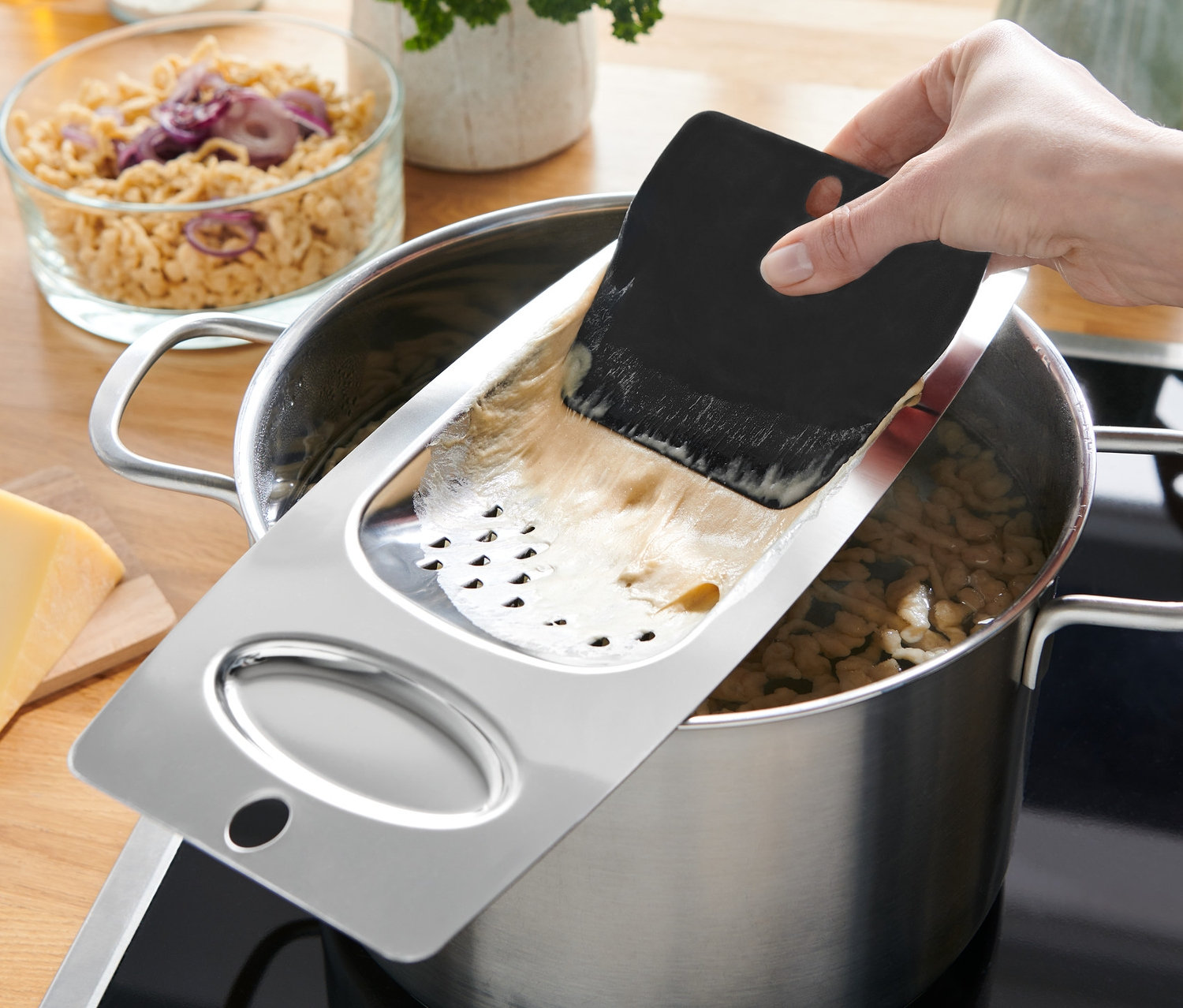 Ręka trzyma tarkę do szpecli nad garnkiem z gotującymi się szpeclami.