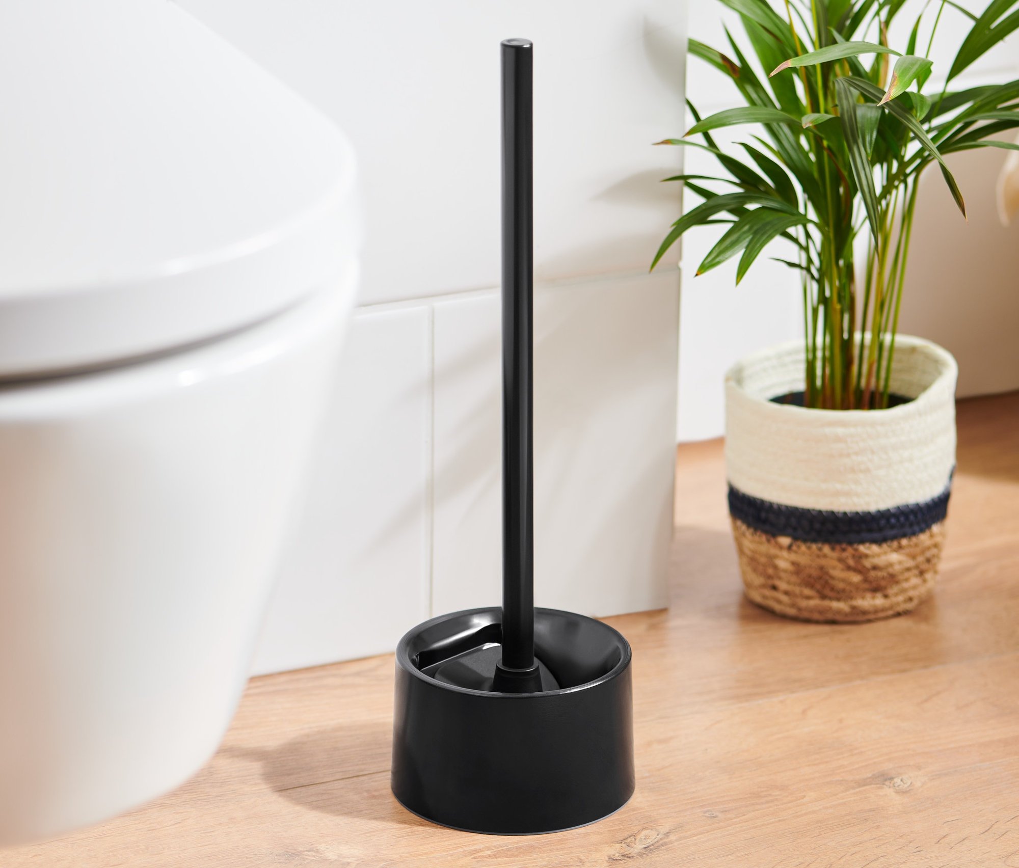 Czarna silikonowa szczotka do WC stoi obok białej toalety.