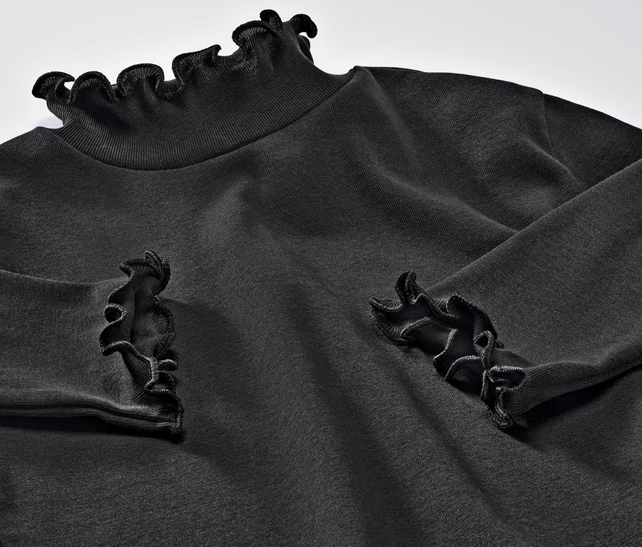 Zbliżenie na dziecięcą koszulkę z długim rękawem z falbankami przy szyi i na nadgarstkach.