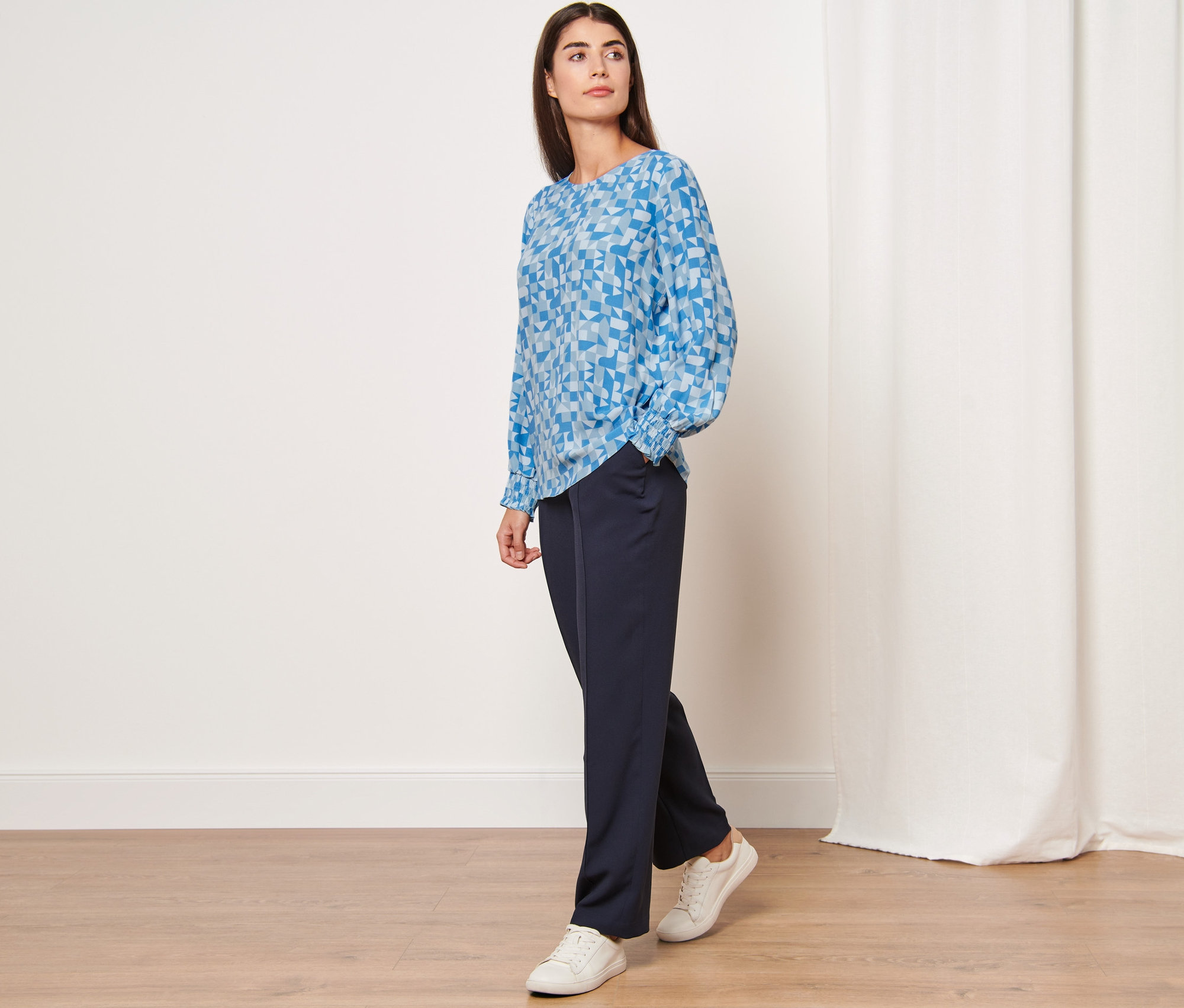 Kobieta pozuje w bluzce z nadrukiem i granatowych spodniach.