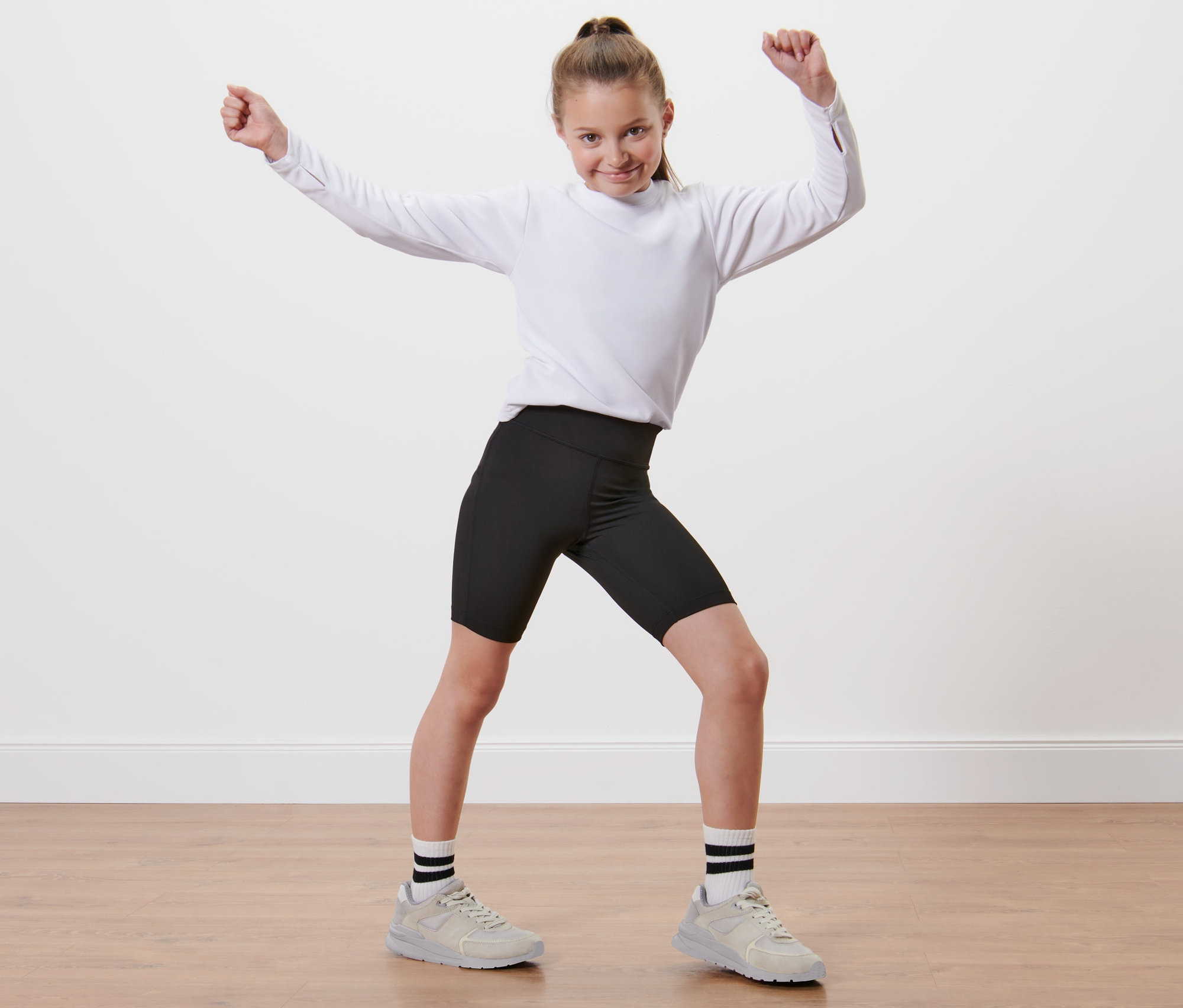 Dziewczyna w białej koszuli i krótkich legginsach stoi z podniesionymi rękami.