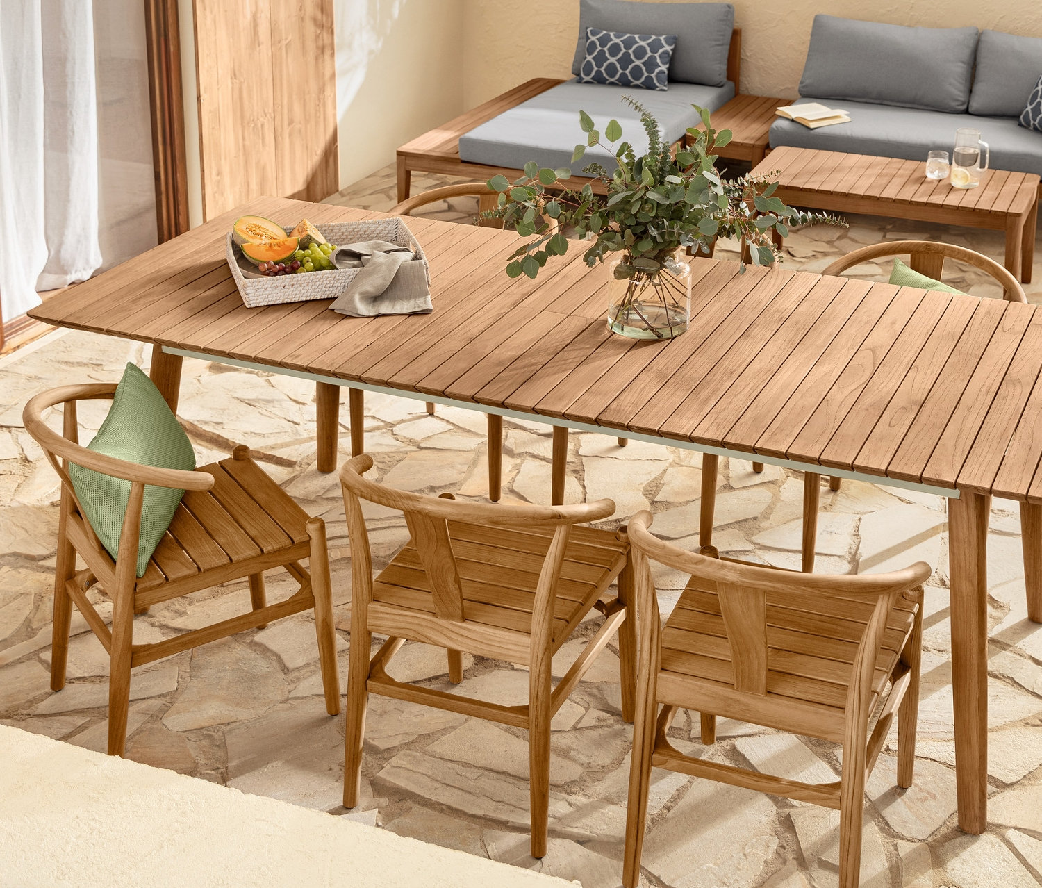 Taraz z teakowym stołem rozkładanym, krzesłami i zestawem wypoczynkowym oraz 2 poduszkami outdoorowymi.