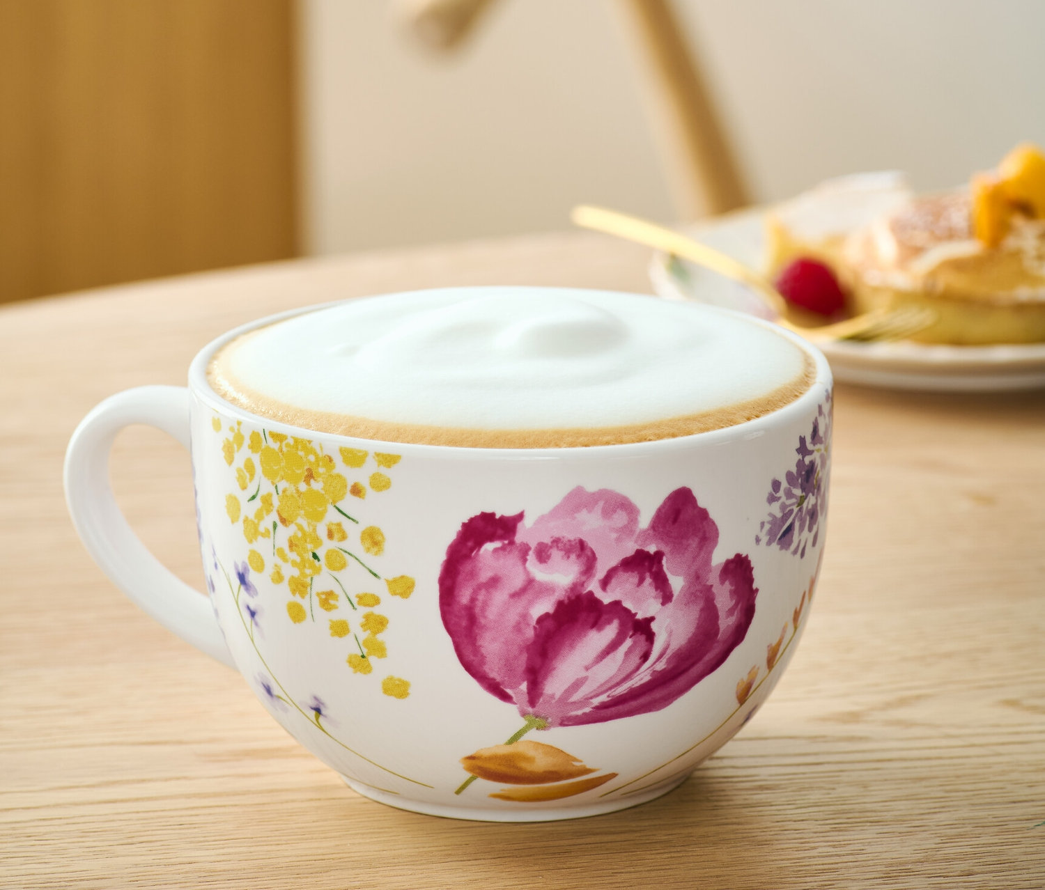 Duża filiżanka w kwiaty z kawą na stole.