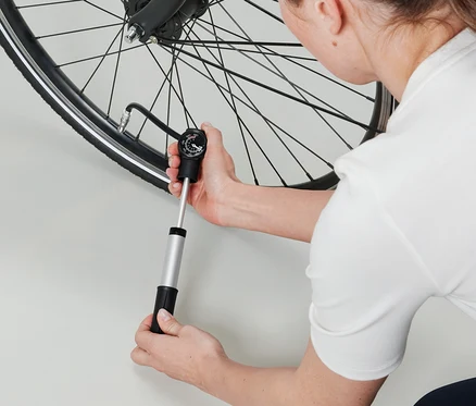 Kobieta pompuje oponę rowerową mini pompką dwudrożną.
