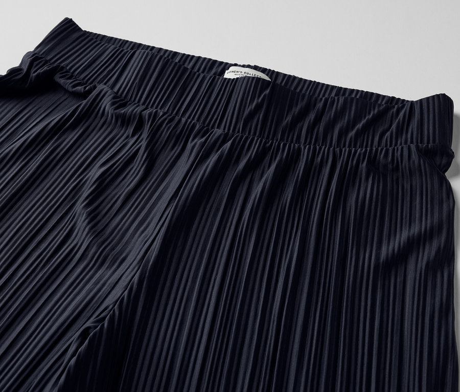 Zbliżenie na granatowe plisowane spodnie.