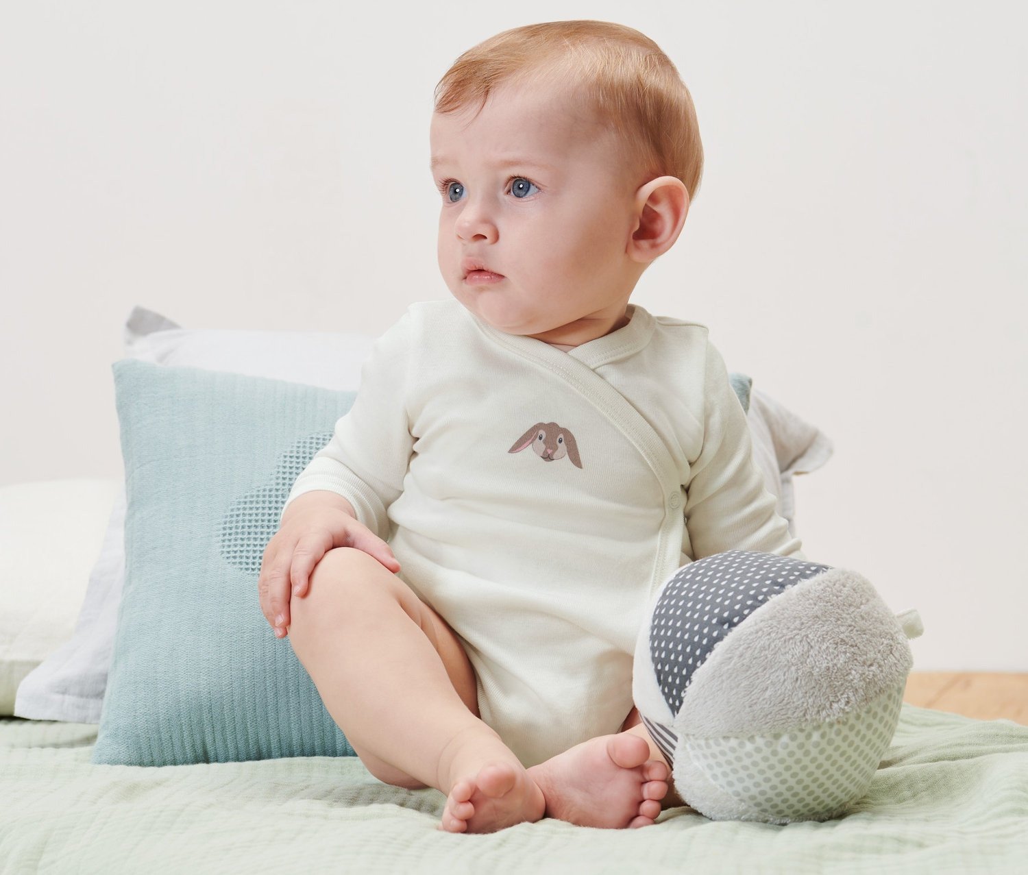 Dziecko siedzi na łóżku i ma na sobie body z długim rękawem, 3 sztuki.