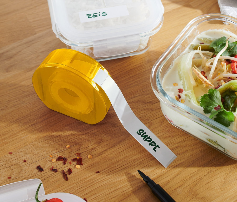 Żółty podajnik do etykiet na drewnianym stole obok pojemników z ryżem i zupą.