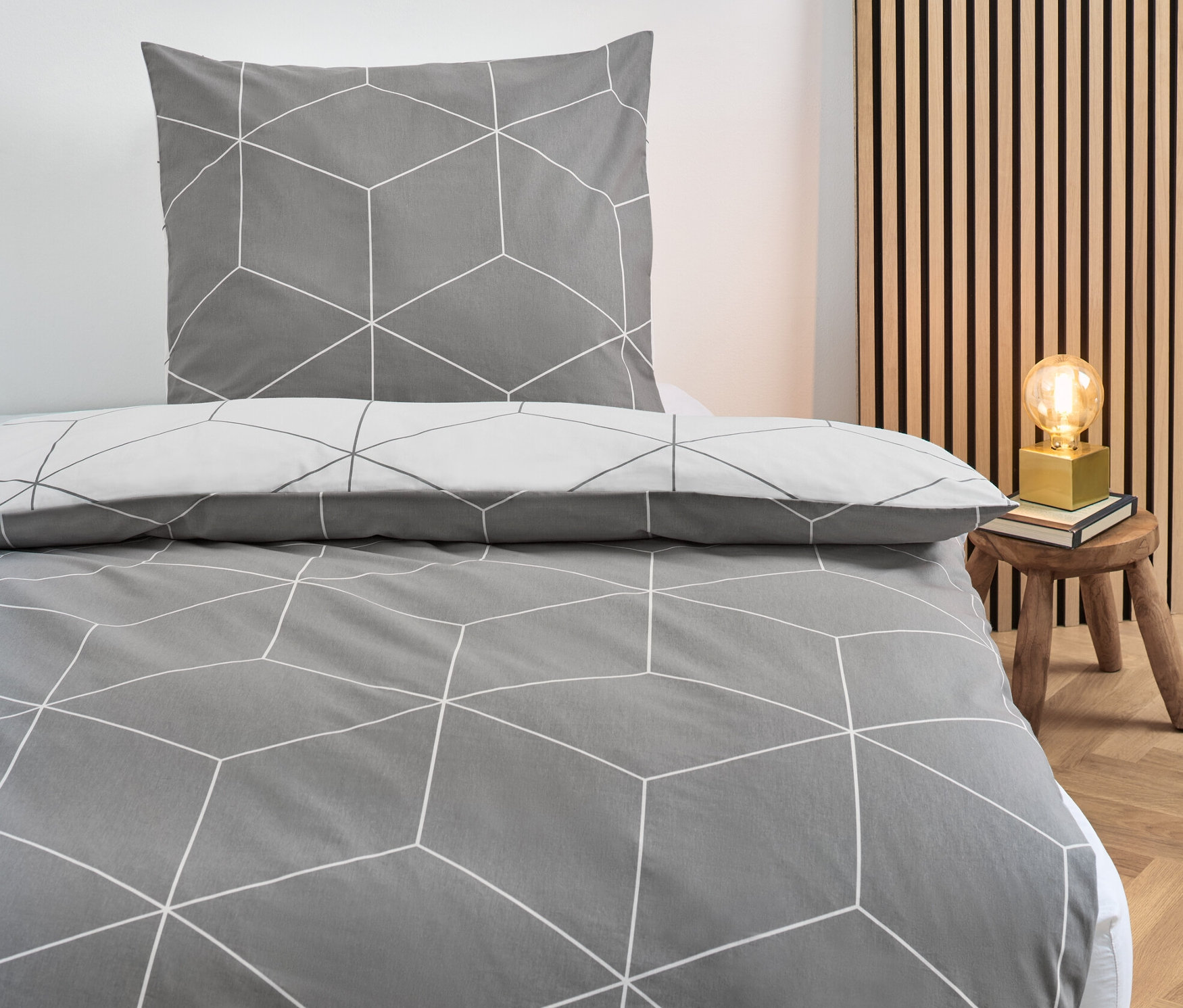 Szara pościel z bawełny renforcé o standardowym rozmiarze z geometrycznym wzorem na łóżku.