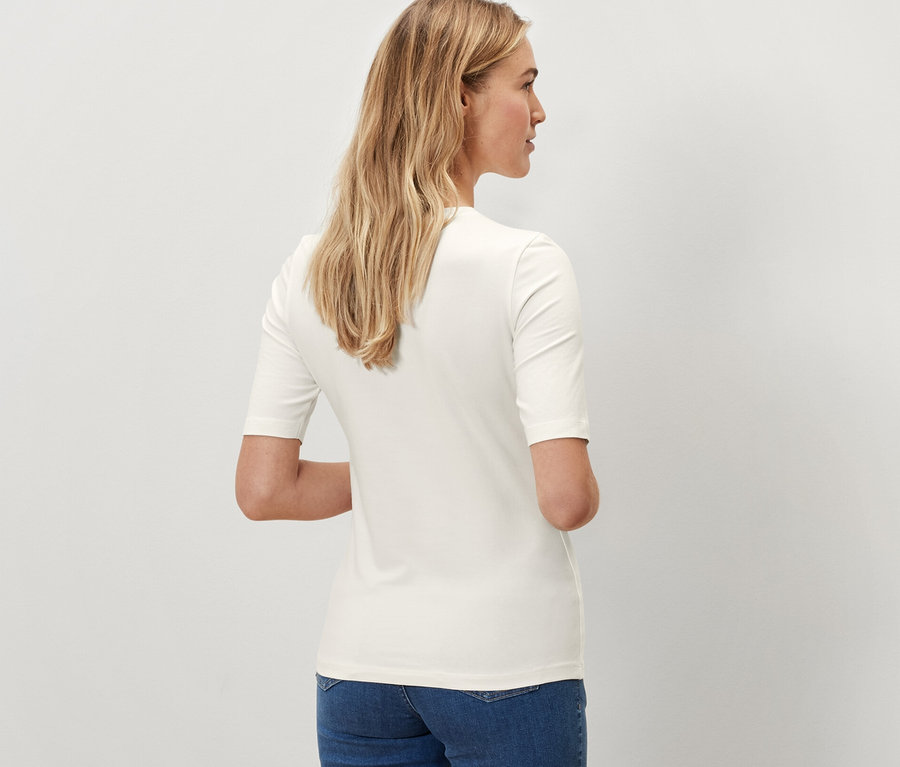 Widok z tyłu kobiety w kremowej koszulce z półdługim rękawem i niebieskich dżinsach.