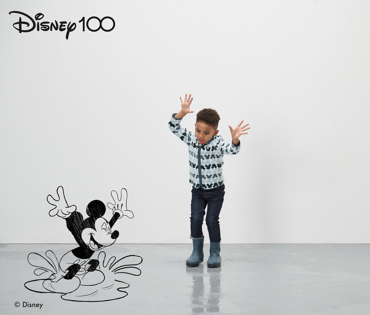 Chłopiec stoi przed narysowaną postacią Myszki Miki i macha rękami. Ma na sobie niebieską kurtkę polarową »Micky«.