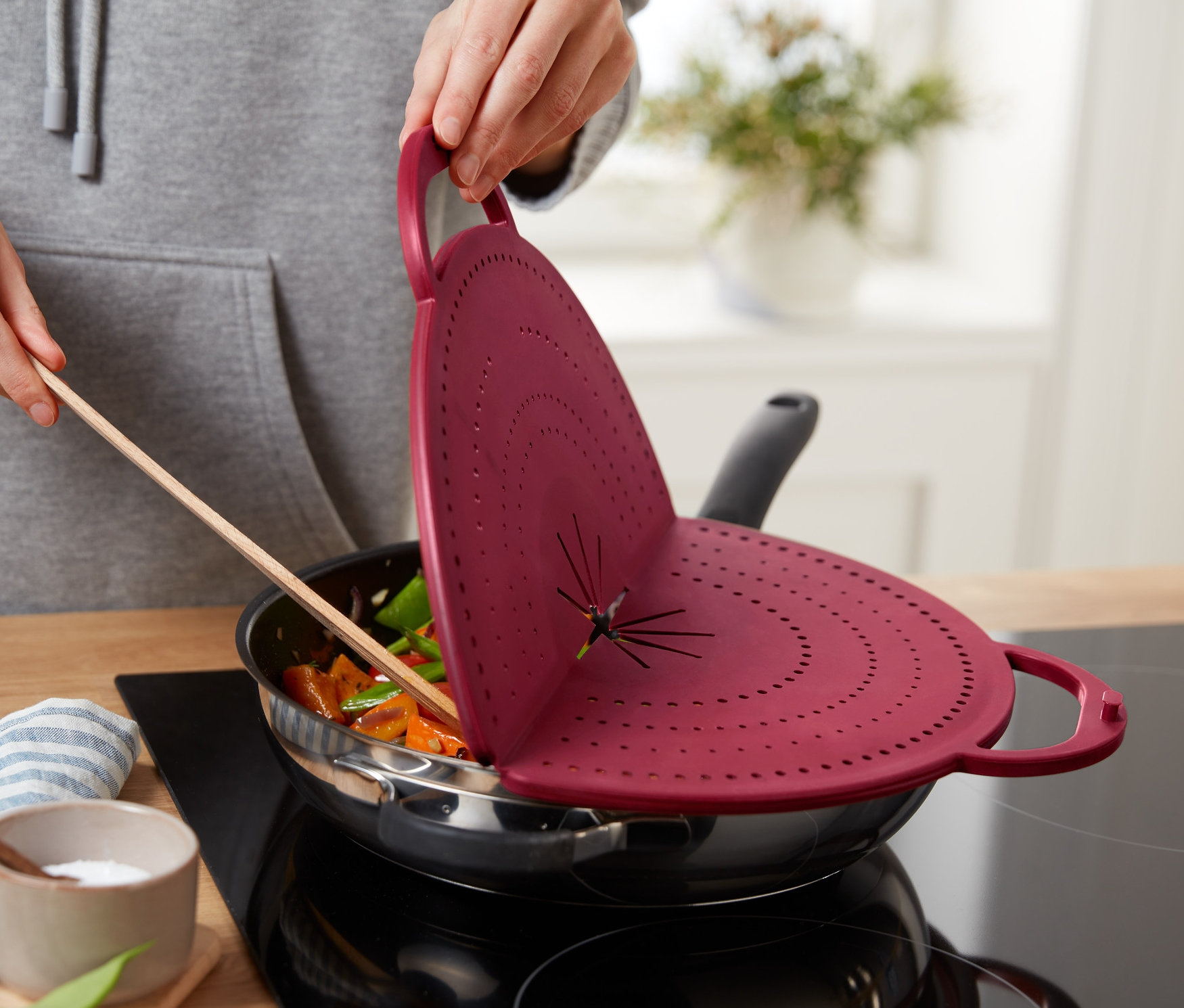 Osoba gotuje warzywa na patelni i trzyma czerwona osłonę na patelnię 4 w 1.