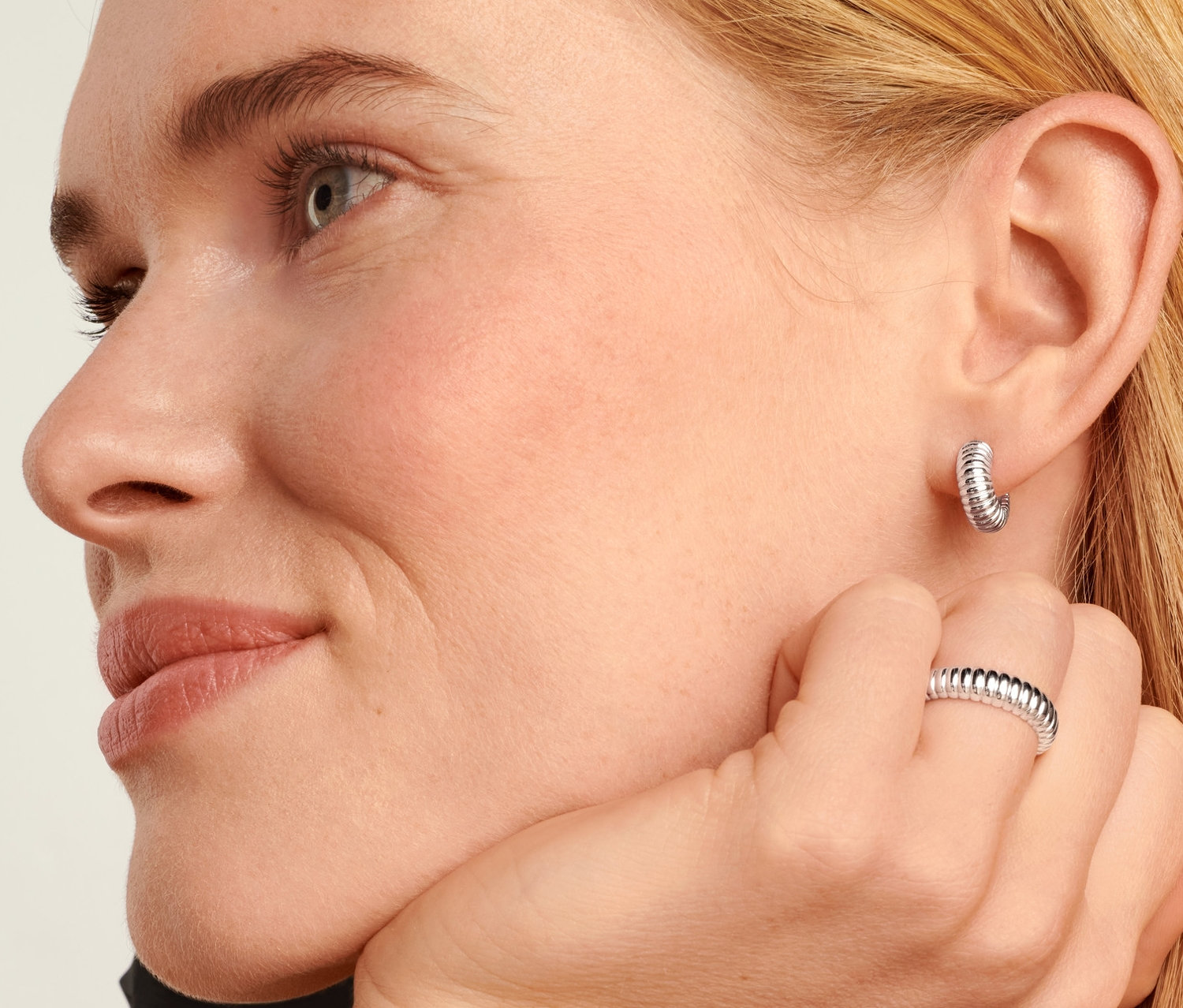 Blondynka ma na sobie srebrne kolczyki kreolki 925 Ribbed i srebrny pierścionek 925 Ribbed.
