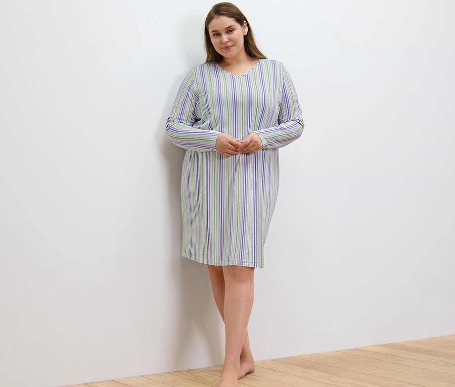 Kobieta w koszuli nocnej w paski stoi przy ścianie.