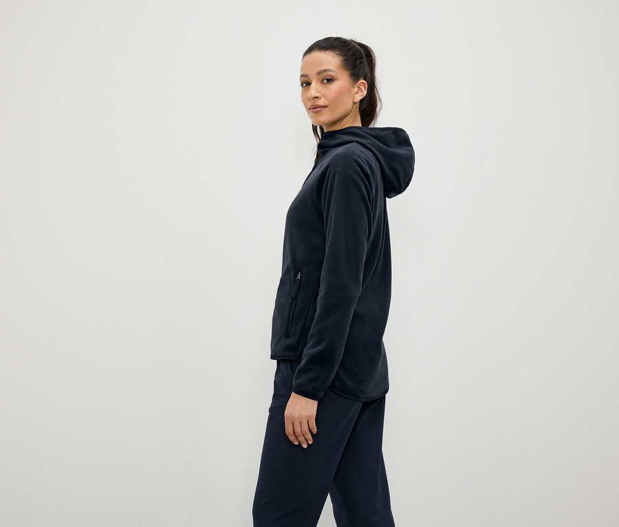 Kobieta w granatowej bluzie polarowej z kapturem i spodniach, stojąca bokiem.