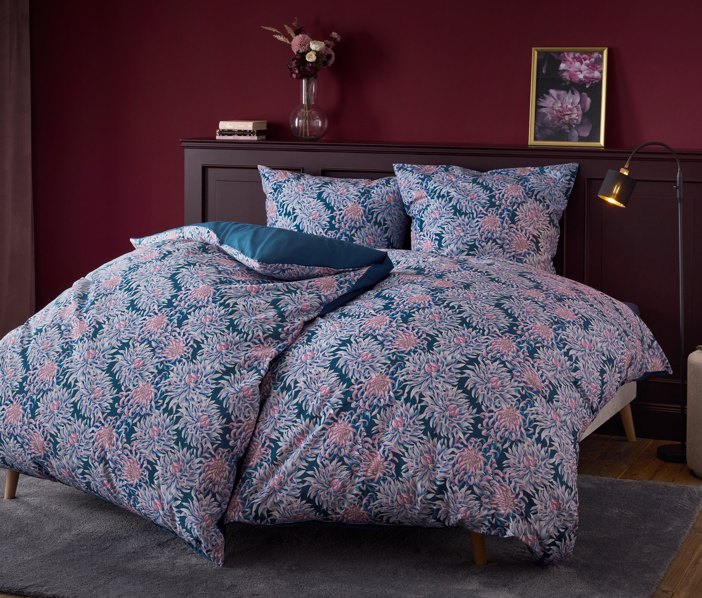 Pościel w kwiaty na łóżku z ciemnym drewnianym zagłówkiem.