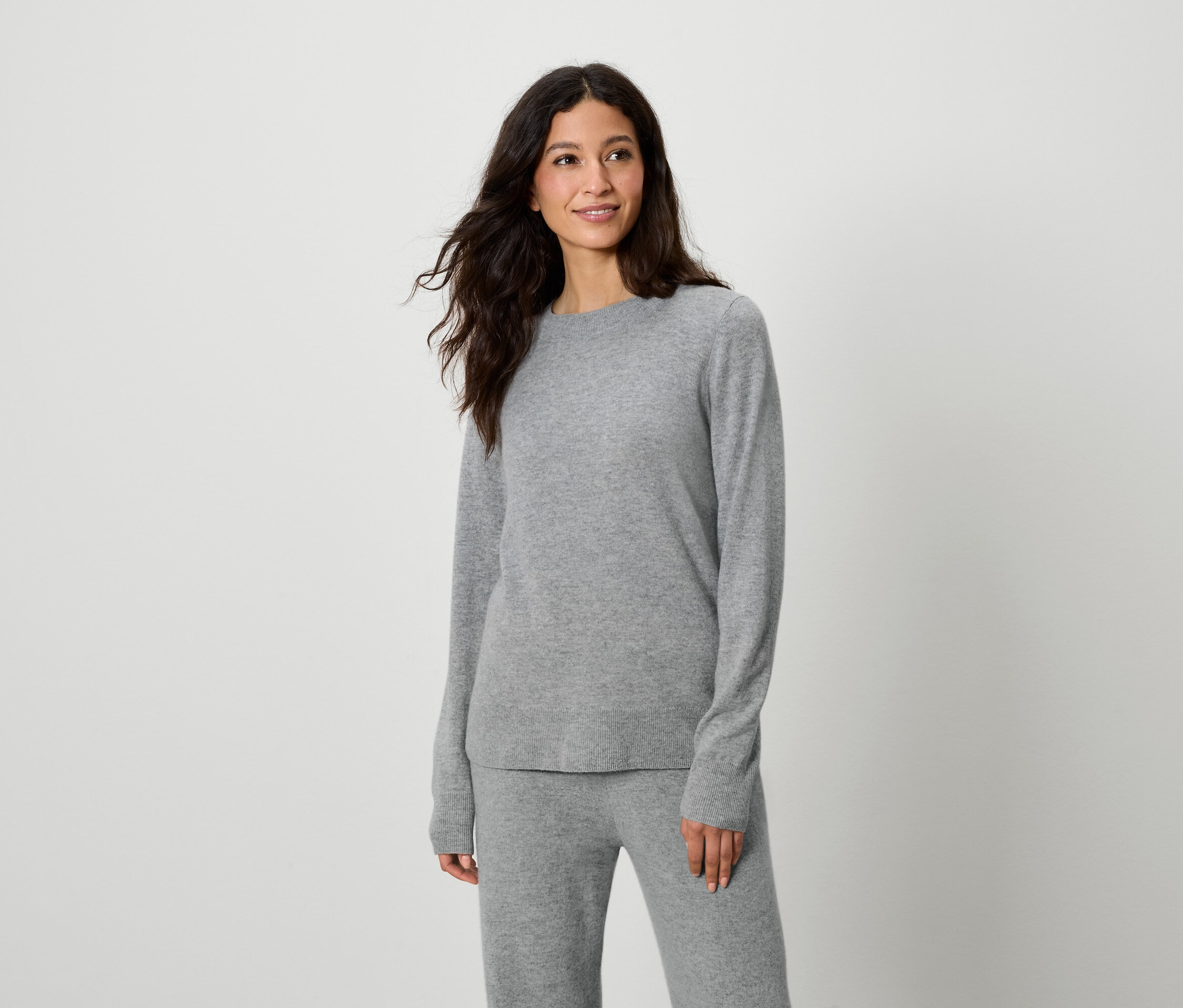 Kobieta pozuje w szarym swetrze i spodniach.