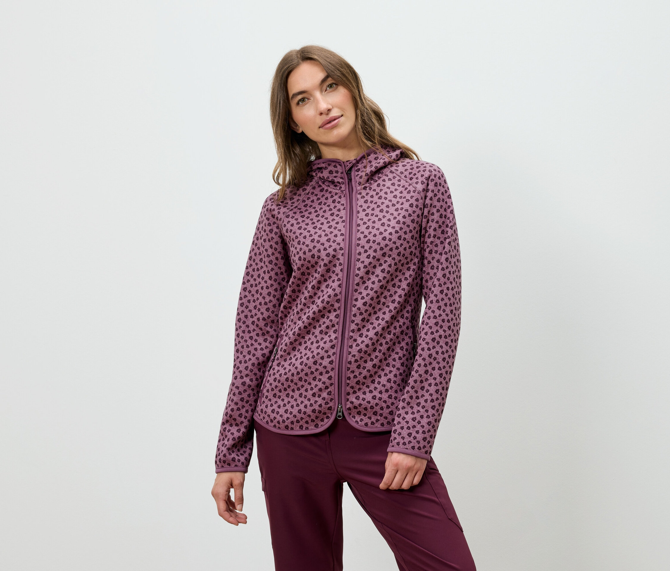 Kobieta pozuje w bordowej bluzie z kapturem i spodniach.