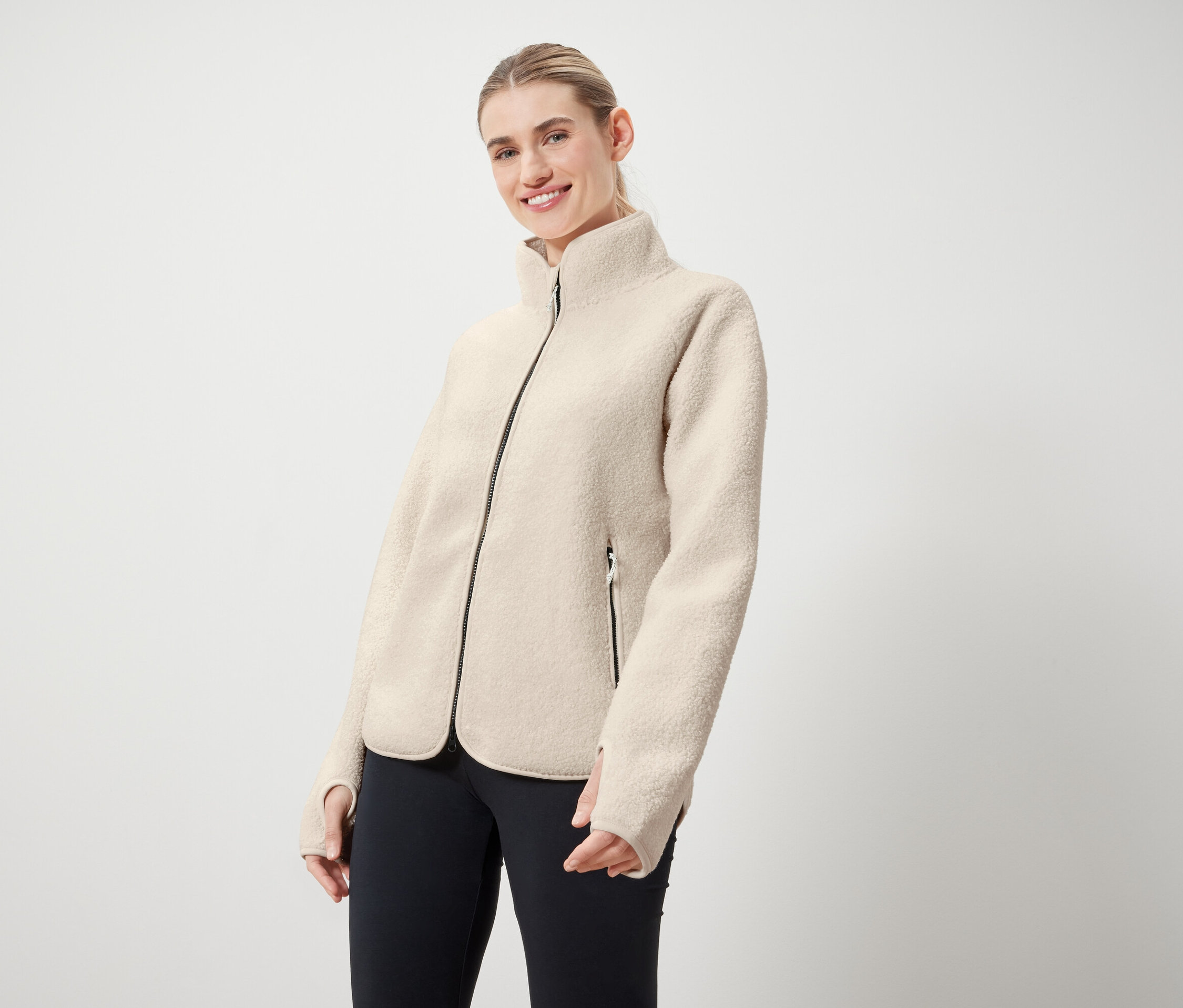 Kobieta ma na sobie kremową kurtkę z czarnym zamkiem i czarne legginsy.
