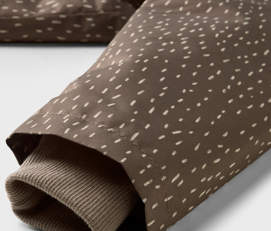 Detal kurtki przeciwdeszczowej termoaktywnej dla dzieci, brązowa tkanina z białymi kropkami i brązowy rękaw.