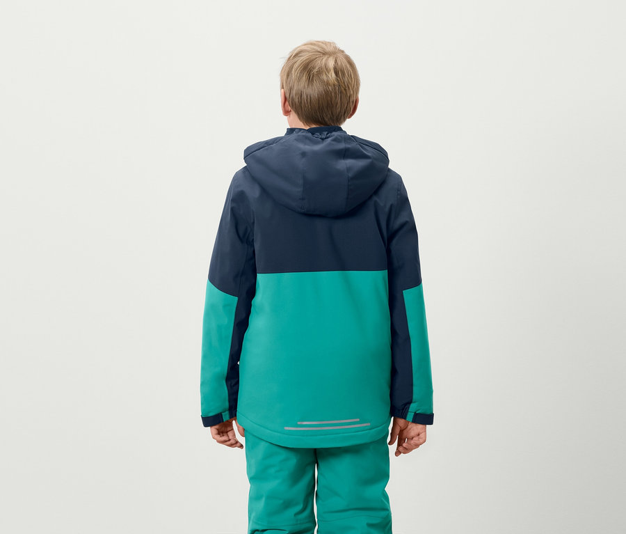 Chłopiec stoi tyłem, ubrany w niebiesko-zieloną kurtkę i zielone spodnie.