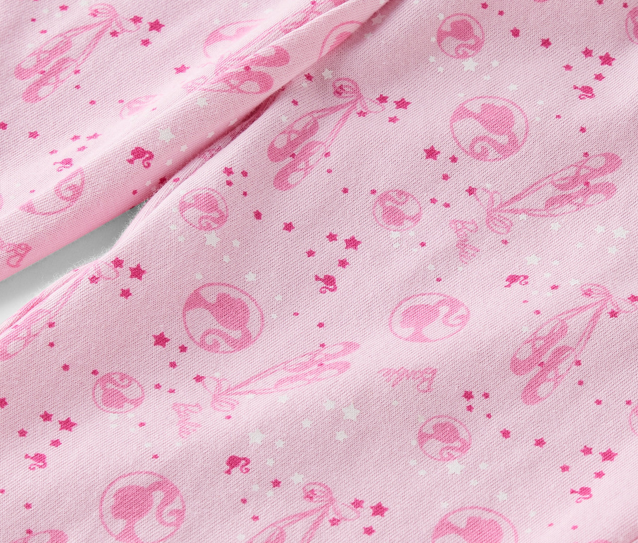 Zbliżenie na różowy materiał zadrukowany baletkami, gwiazdkami i sylwetkami Barbie.