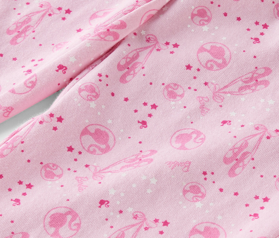 Zbliżenie na różowy materiał zadrukowany baletkami, gwiazdkami i sylwetkami Barbie.