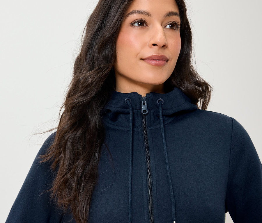 Kobieta ma na sobie granatową bluzę z kapturem zapinaną na zamek błyskawiczny.