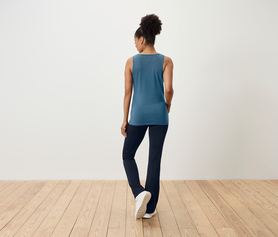 Kobieta tyłem do kamery ma na sobie niebieski top i granatowe spodnie.