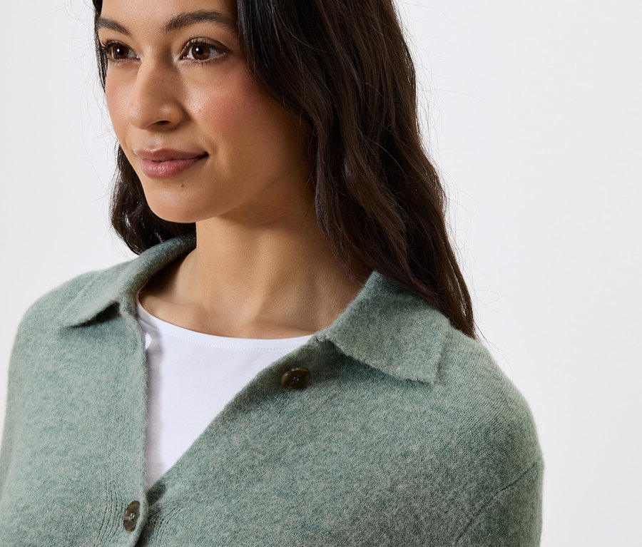 Portret kobiety o ciemnych włosach w zielonym swetrze z kołnierzykiem i guzikami.