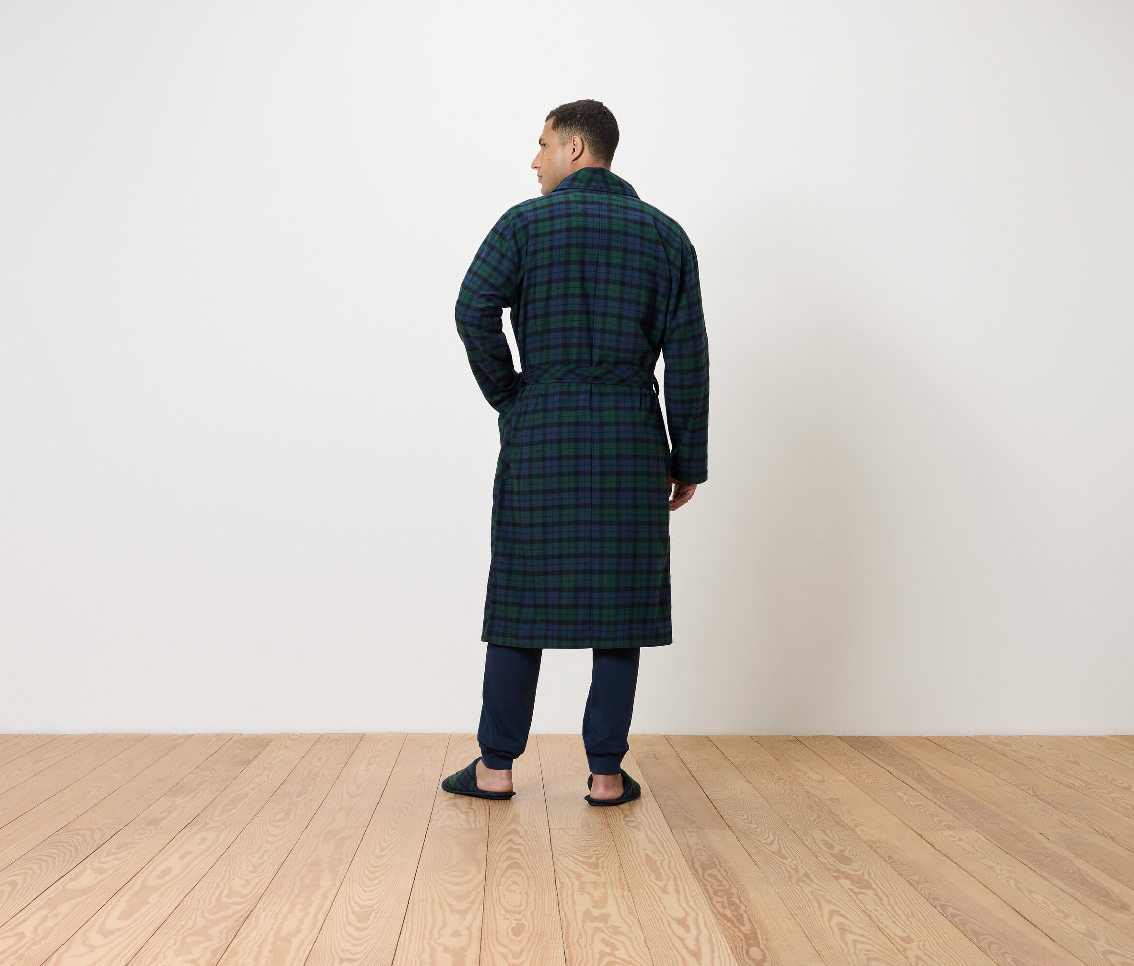 Mężczyzna tyłem do kamery ma na sobie długi, kraciasty szlafrok i ciemne spodnie.