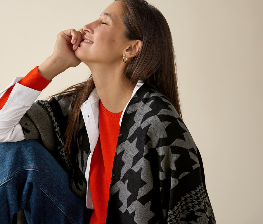 Kobieta siedzi i ma na sobie pomarańczowy, cienki sweter z wełny merino.