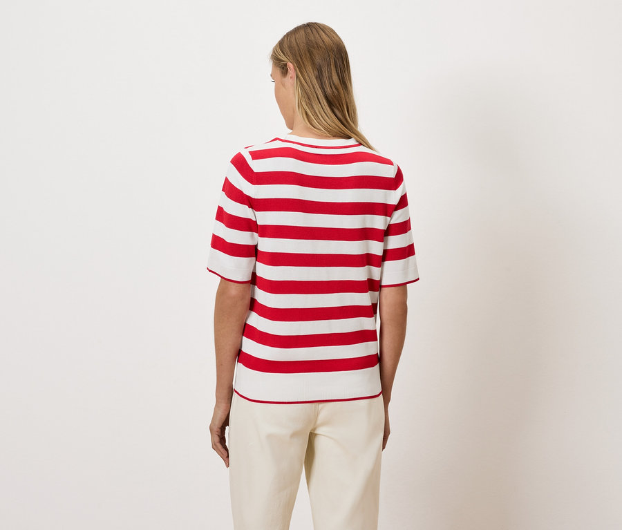 Kobieta tyłem do aparatu ma na sobie bluzkę w czerwono-białe paski.