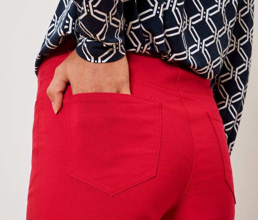 Kobieta wkłada rękę do tylnej kieszeni czerwonych spodni.