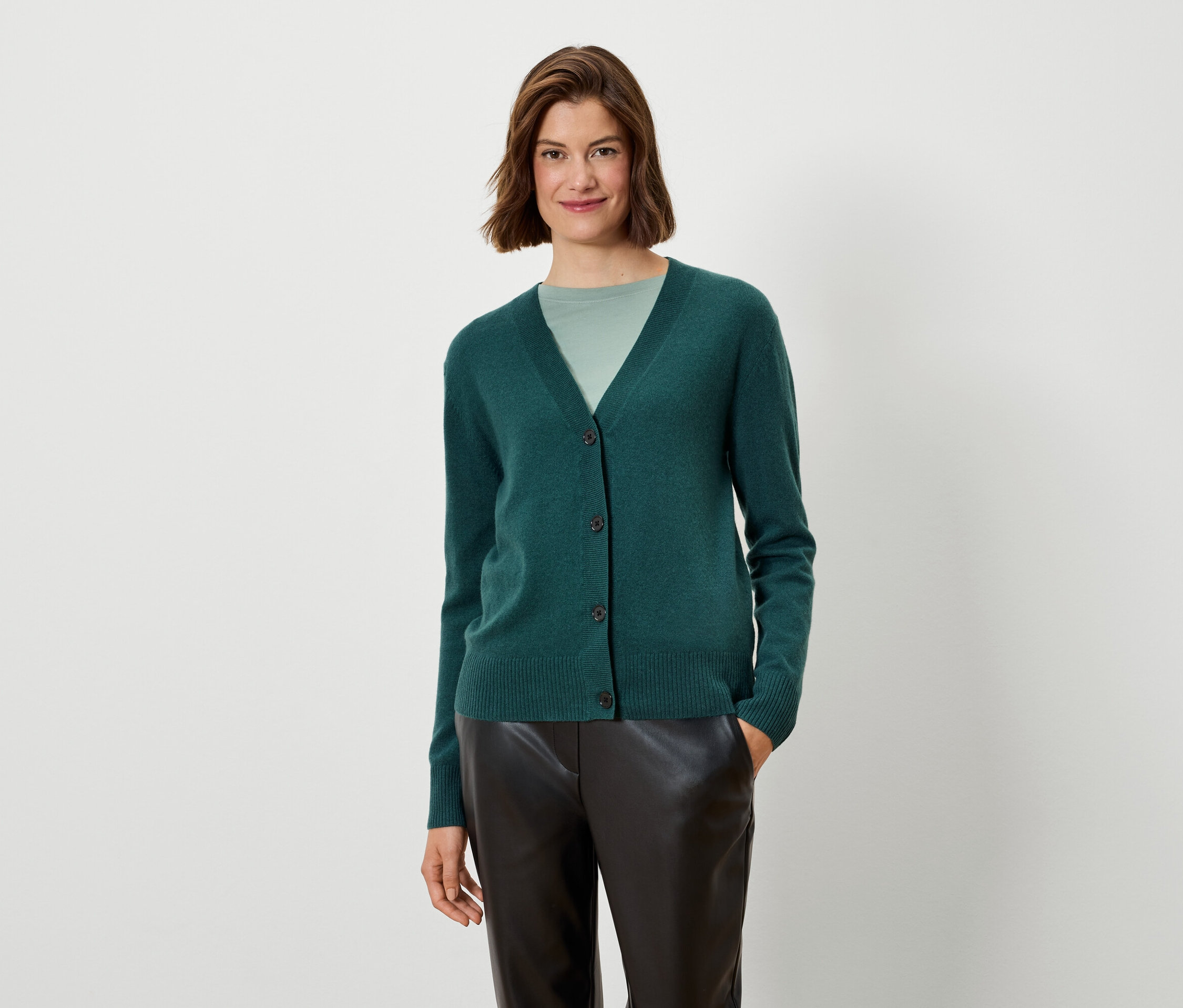 Kobieta ma na sobie zielony kardigan i czarne spodnie.