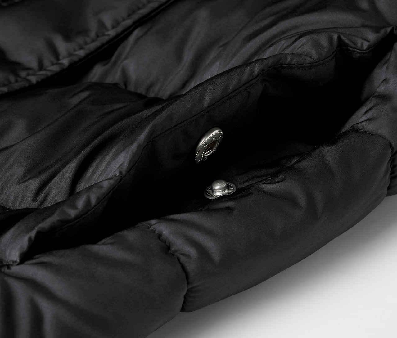 Zbliżenie na czarną kurtkę puchową z otwartą kieszenią i dwoma srebrnymi zatrzaskami.