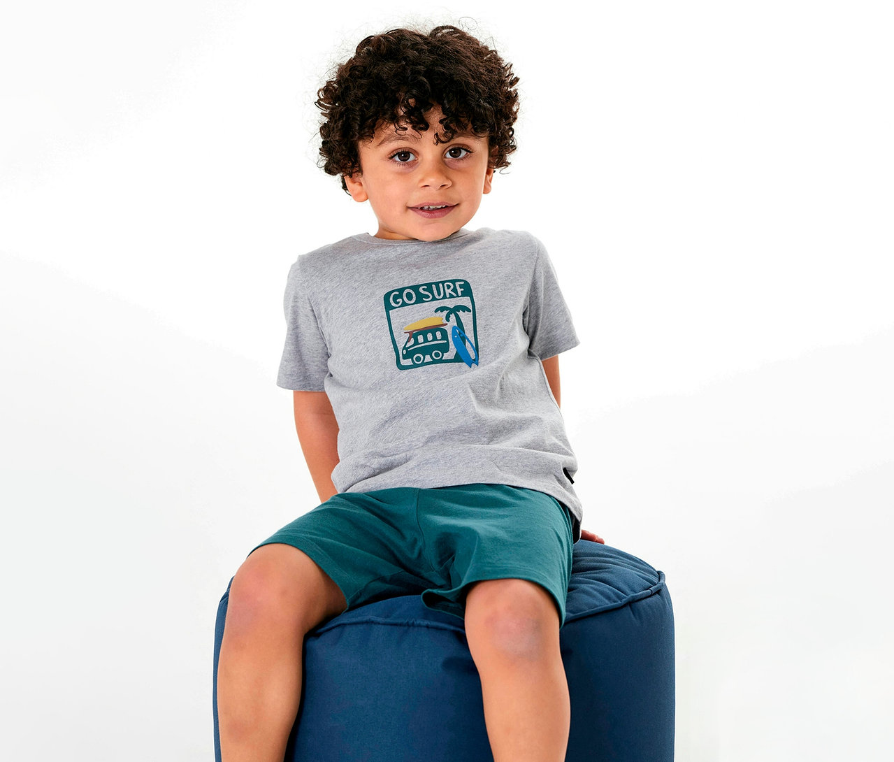 Chłopiec siedzi na pufie, ubrany w piżamę dziecięcą SCHIESSER.