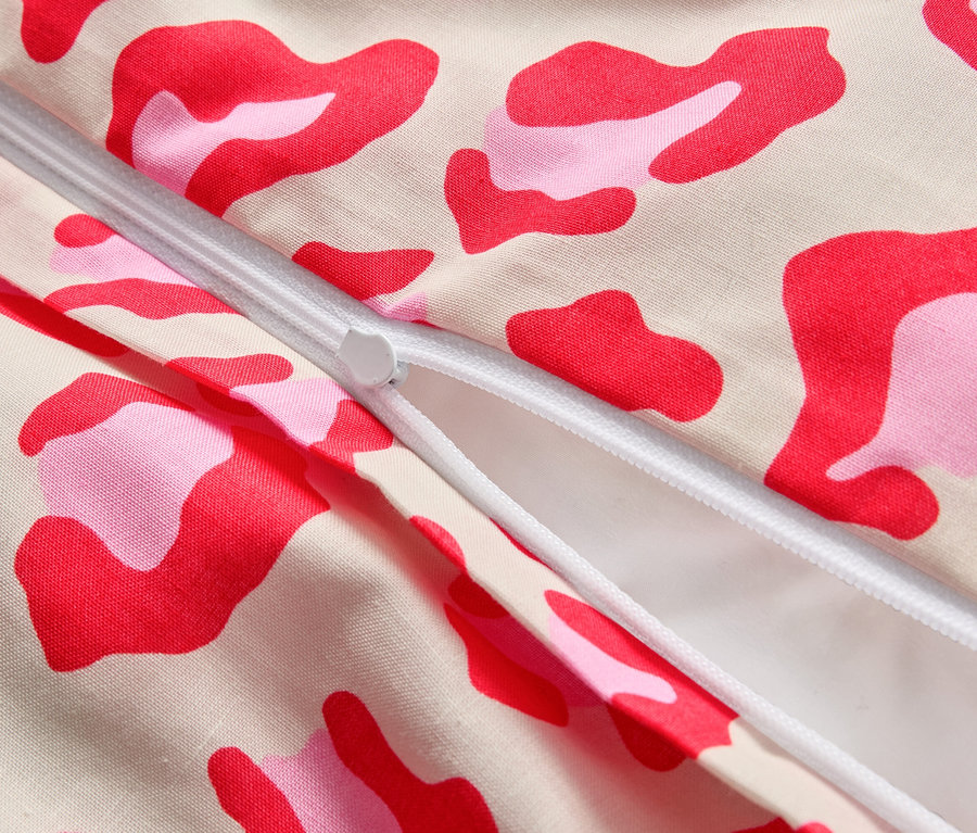Zbliżenie częściowo otwartego zamka błyskawicznego na tkaninie w różowe i czerwone plamy.