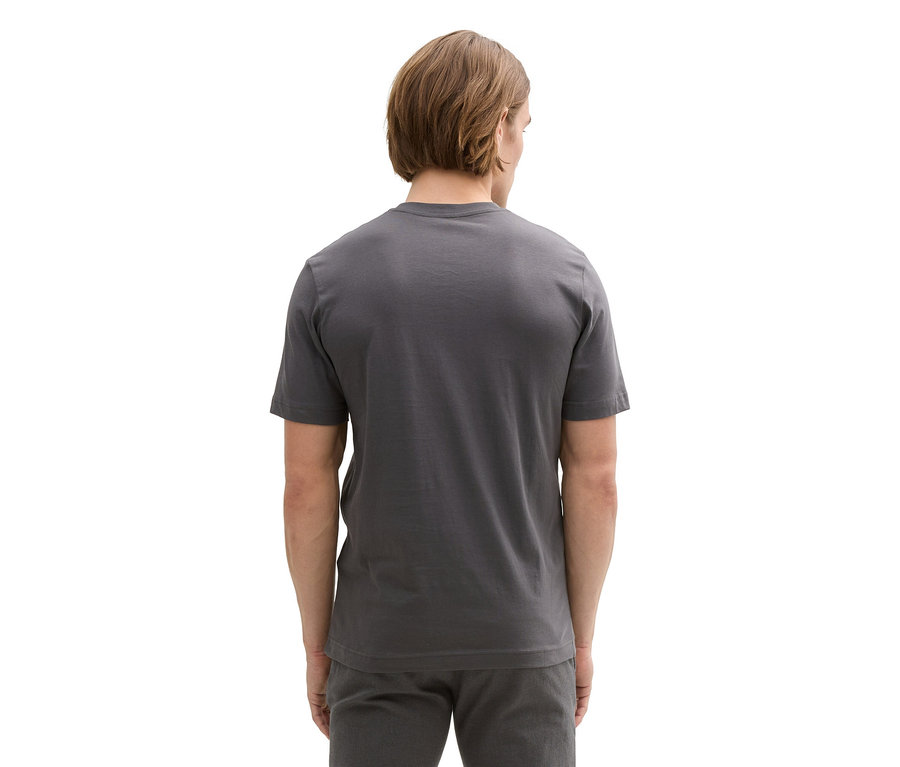 Mężczyzna od tyłu w szarym T-shircie z logo Tom Tailor i szarych spodniach.
