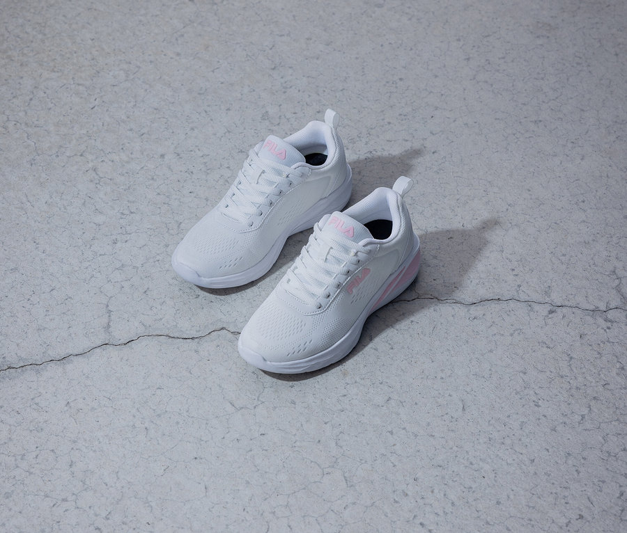Dwa białe tenisówki Fila z różowym logo leżą na szarym tle.